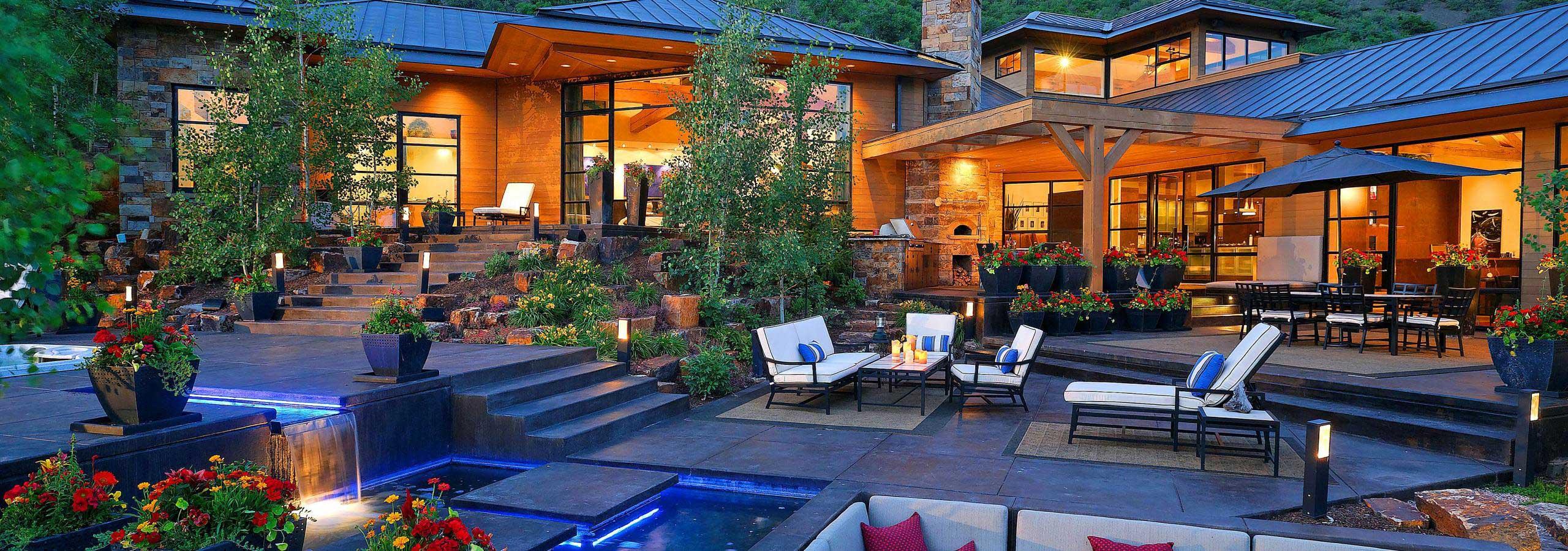 Lit home terrace with pool, fire pit and lounge seating at dusk